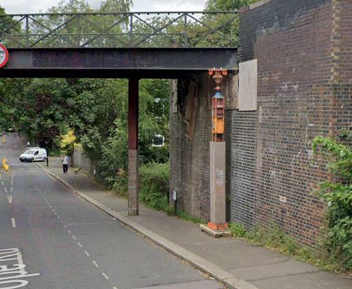 A street with a bridge over a brick wallDescription automatically generated